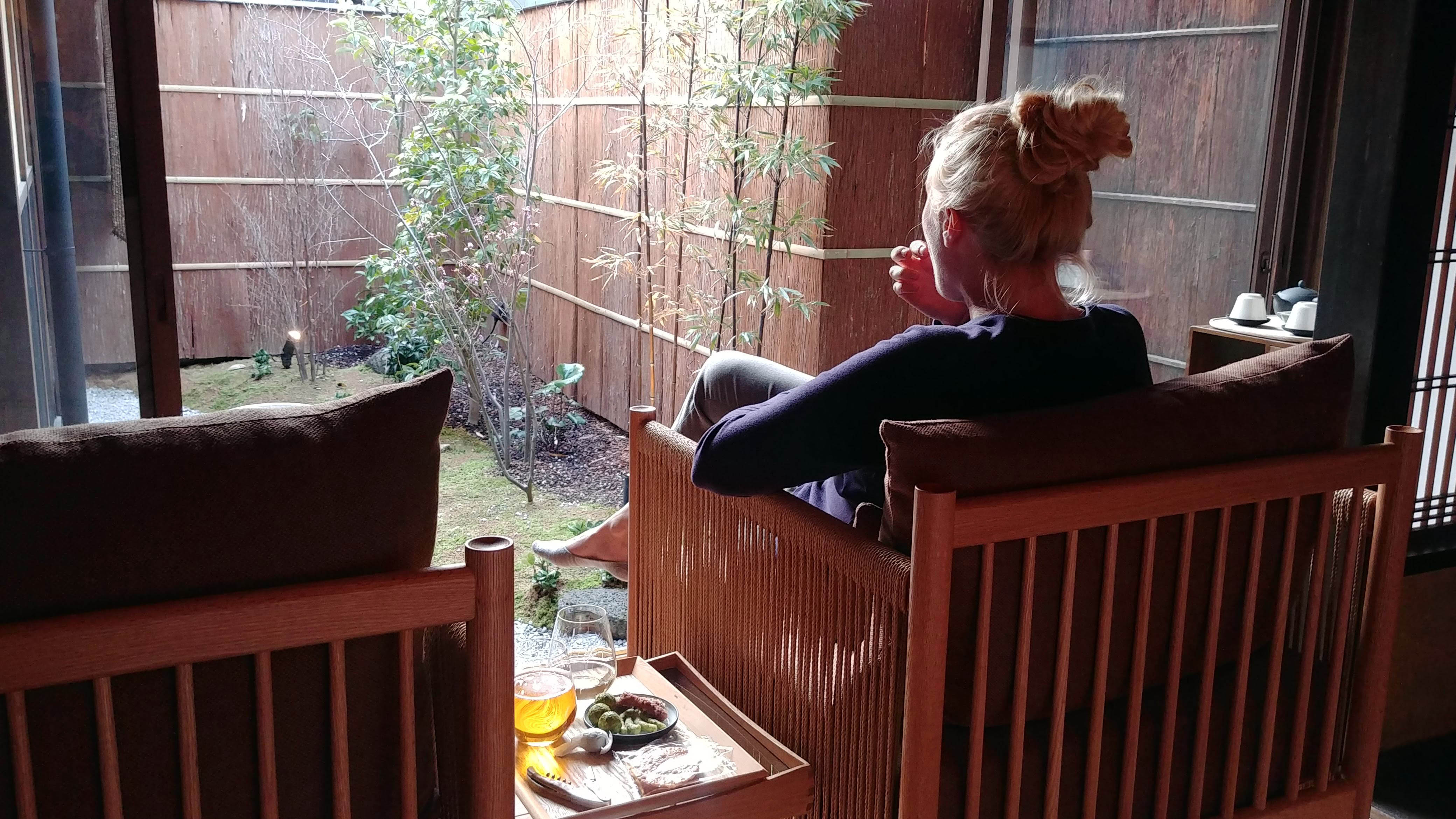 A person seated on a ryokan veranda in Kyoto, looking out at a small enclosed garden with a tea set beside them
